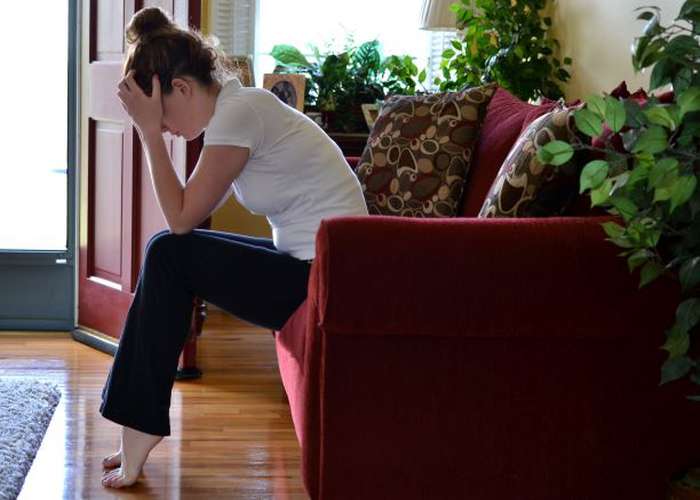 Stressed woman sitting on couch, putting her hands on her front head, and showing signs of stress and anxiety.