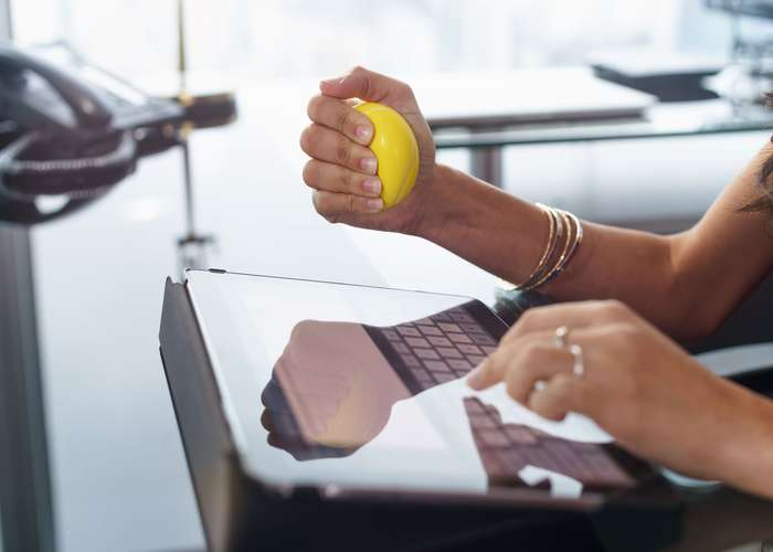 Manage stress for Alzheimer: a woman pressing on a stress ball in front of a desk.