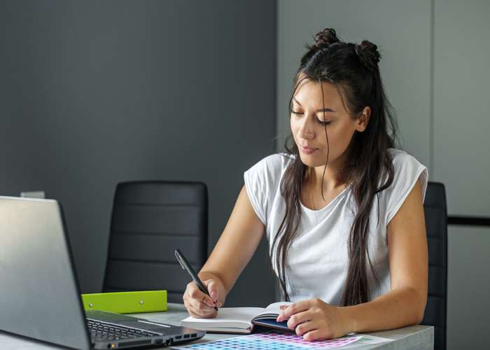 End distraction for ADHD: woman focusing on her work, sitting on a desk in front of laptop.