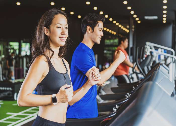Exercise regularly for ADHD: couple exercising at the gym, running on treadmills.