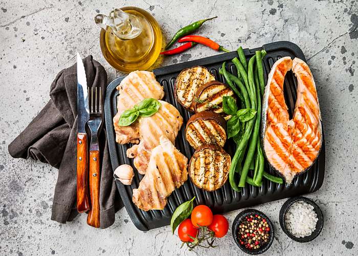 Eat grilled or baked foods for IBS: selection of grilled foods on a metal barbecue plate.