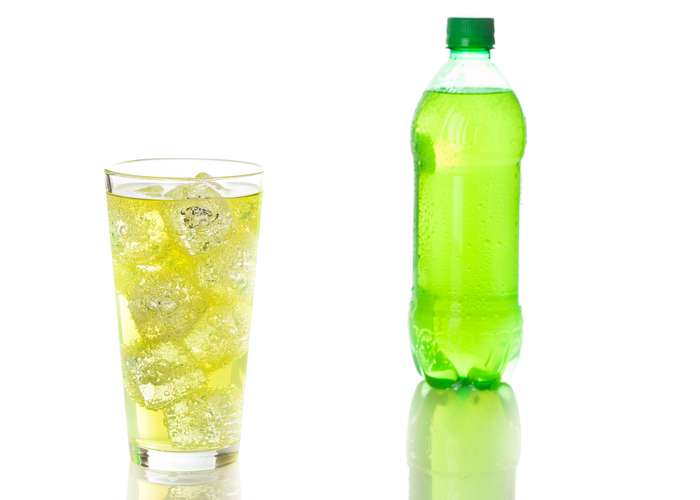 Avoid energy drinks for ADHD: Green energy drink in a glass with ice cubes, and a full energy bottle next to it.