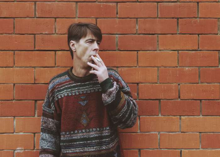 Avoid smoking for Alzheimer: Man smoking a cigarette standing in front of a wall.