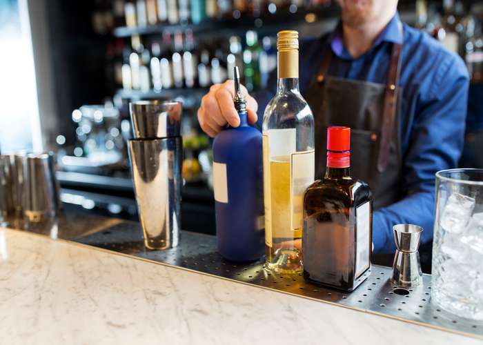 Avoid excess alcohol for Alzheimer: man standing behind a bar full of alcohol.
