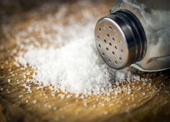Avoid salt for heart disease because it increases blood pressure: salt shaker, and salt grains on a table.