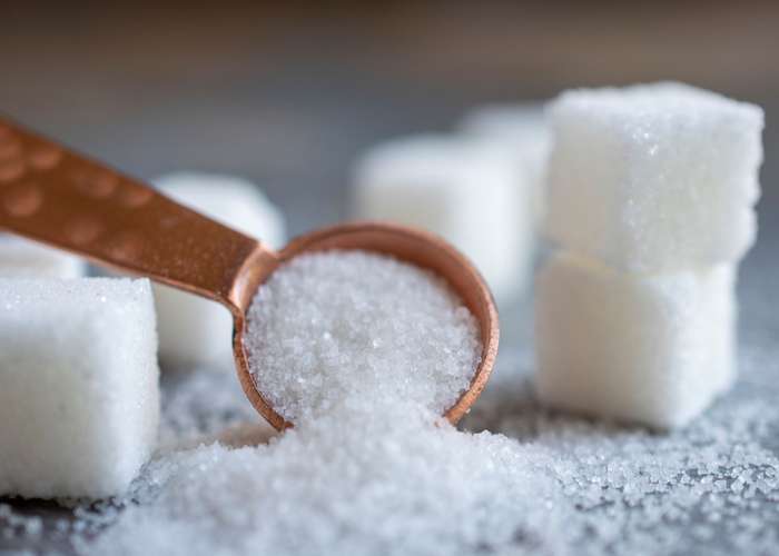 Limit sugar for arthritis: grains of sugar in a spoon and sugar cubes next to it.
