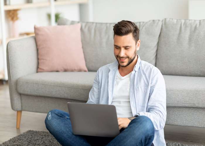Avoid prolonged sitting for hemorrhoids: man sitting on floor, working on laptop.
