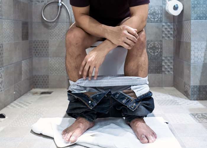Avoid straining to poop for hemorrhoids: man sitting on toilet seat.